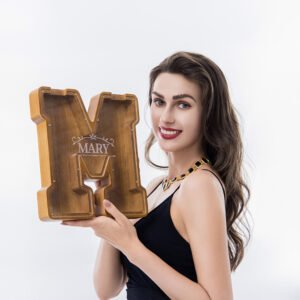 Woman holding custom engraved large walnut wooden letter piggy bank, personalized initial money box for birthday/holiday gift