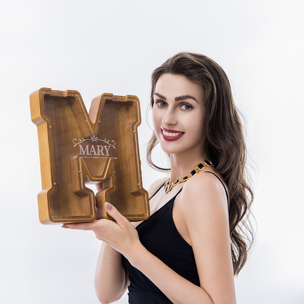 Woman holding custom engraved large walnut wooden letter piggy bank, personalized initial money box for birthday/holiday gift