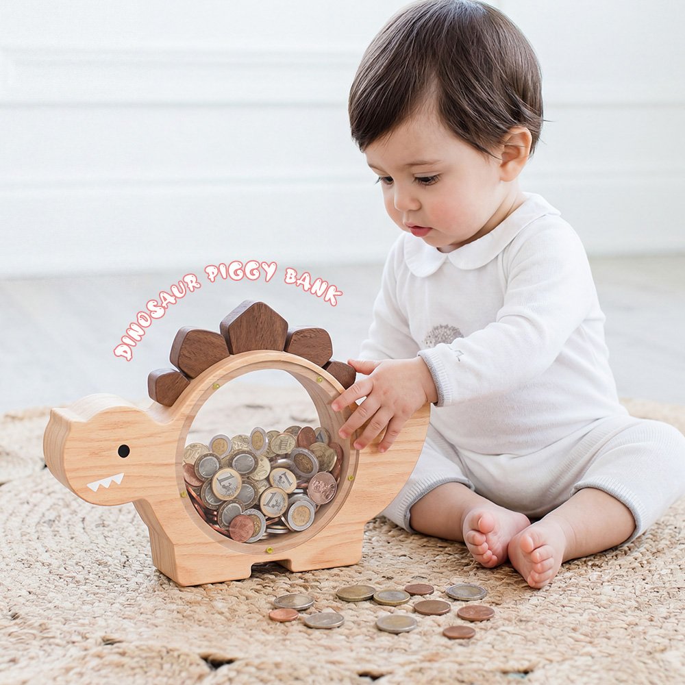 Natural wood dinosaur piggy bank with a clear acrylic front. A child's hand is dropping a coin into the top slot, complete with fun alphabet stickers for DIY decoration-2.