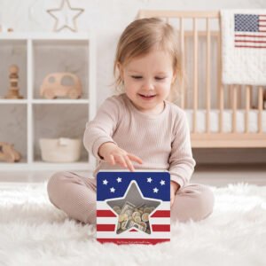 A happy toddler girl sitting on the floor playing with her USA flag design money box, making it a perfect patriotic gift for kids.